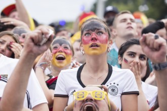 A woman wearing make-up in the German national colours watches the football match in the fan zone