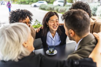 Successful team of multi-ethnic business people celebrating embracing form the shoulder sitting in