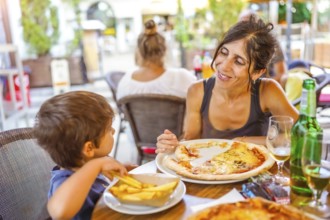 Mother and son sharing a meal of pizza and french fries at an outdoor restaurant, enjoying their