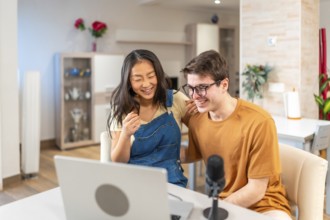 Asian woman and caucasian man smiling while engaging in a fun activity at home, showcasing a joyful