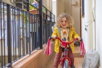 Little blonde cute girl learning to ride a bike in the terrace at home