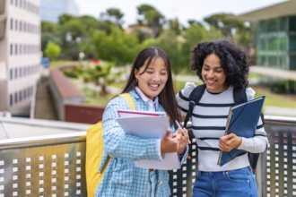 Two beauty young smiling multi-ethnic students reading notes standing outside the university campus