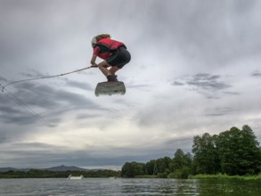 Boy or girl flies over the lake, jump with wakeboard, red life jacket, water skiing in wakepark,