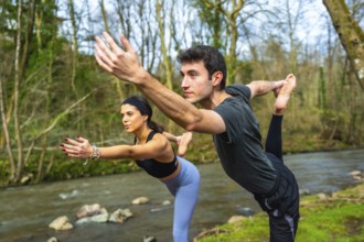 Yoga instructors performing a balancing pose by a river, showcasing flexibility and mindfulness in