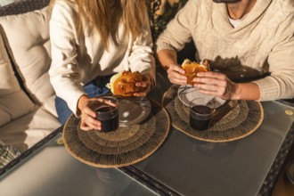 Couple sharing a relaxed moment, eating burgers and drinking beverages at a glass table, creating a