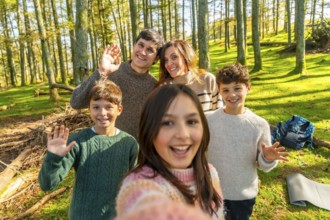 Caucasian family taking selfie and waving at camera standing in an alpine forest enjoying nature