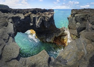 Panoramic view of rugged lava rock formations with a natural arch over turquoise sea under blue