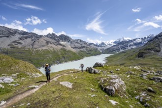 Two mountaineers on a hiking trail at a blue mountain lake, reservoir Lac des Dix, behind mountain