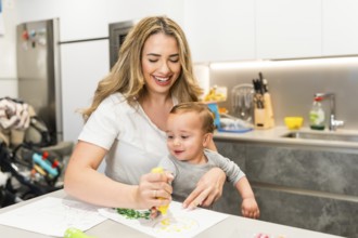 Happy mother and her baby son enjoying creative time, painting together in their bright modern