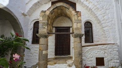 Entrance of a building with ancient columns and a round arch, surrounded by flowers and stone