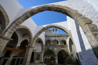 Inner courtyard of a monastery with stone arches and Mediterranean architecture under a blue sky,