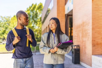 Two african and chinese multi-ethnic friends talking walking along university campus carrying