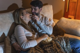 Couple enjoying a cozy night in, sharing popcorn and watching a movie together on the sofa