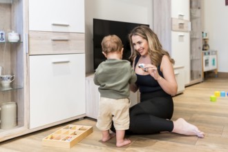Smiling mother showing toy car to her baby boy while playing together on the floor in the living