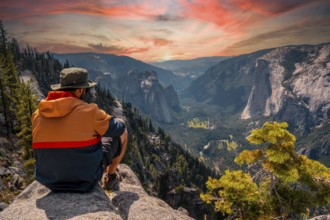 A young man on the trek sitting on the Sentinel Dome lookout in Yosemite National Park looking at