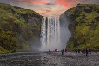Group of tourists looking at the beautiful rainbow at the impressive Skogarfoss waterfall in