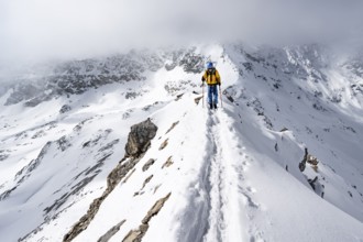 Mountaineer climbing up the narrow ridge of Piz Laviner, view of wintry mountain landscape, Grisons