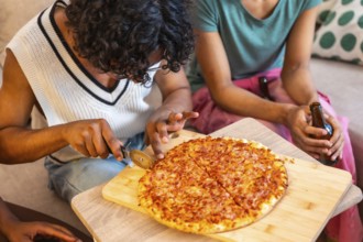 Close-up of man cutting homemade pizza to share with friends at home