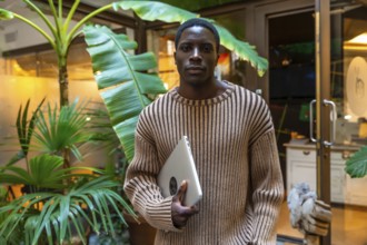 African handsome man with casual clothes carrying laptop standing next to a coworking