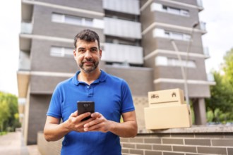 Delivery man using mobile phone standing outdoors next to some boxes to deliver