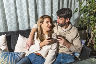 Romantic couple enjoying a glass of wine together, embracing on a comfortable sofa on their terrace