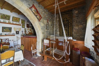 A traditionally furnished interior with stone walls, a wooden ceiling and a loom in the centre,