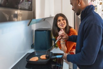 Happy multiethnic couple preparing burgers in a pan in their modern kitchen, enjoying their time