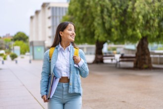 Happy asian university student walking along he campus smiling and looking aside