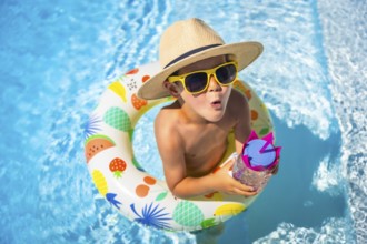 Top view of an expressive caucasian boy wearing sunglasses and sun hat playing inside a pool with
