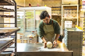 Latin young male baker kneading the raw dough in the kitchen of an artisan workshop