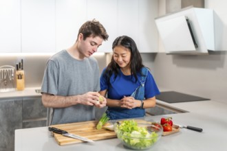 Multiethnic couple joyfully preparing a vibrant, healthy salad together in their modern kitchen,