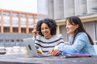 Happy multi-ethnic female students using laptop sitting on the campus