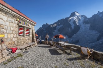 Moutain hut Cabane de l'A Neuve, tourists sitting on terrace, Aiguille Rouges du Dolent massif at