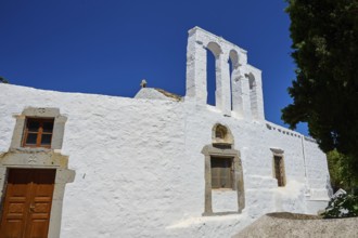 White church with bell tower and wooden door in front of a bright blue sky, Chora, Old Town,