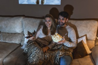 Young couple enjoying a movie night at home, sharing popcorn and relaxing on the sofa under a