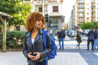 Latin young woman carrying bag in the city holding phone and looking at directions