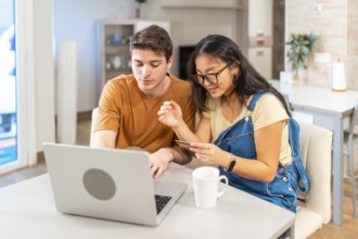 Multiethnic couple making online purchases using laptop and credit card, enjoying a convenient and