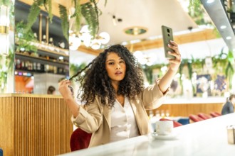Latin sensual woman touching her curly hair while taking selfie at cafeteria