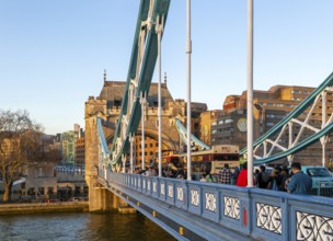 People and open top tour buses cross Tower Bridge in late afternoon, London, England, UK