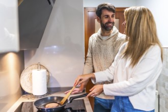 Happy couple preparing dinner together, cooking meat in a pan on the stovetop in their modern