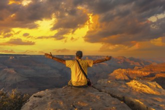 A young man sitting with his hands open and wearing a yellow shirt at Sunset at the Powell Point of