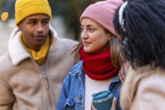 Three friends are chatting and laughing together on a cold winter day in the city, enjoying each