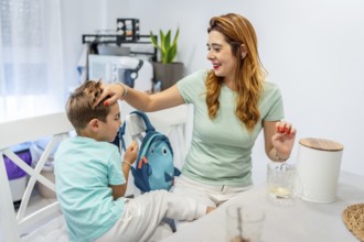 Tender caucasian mother sitting on the kitchen stroking her son's head before he goes to school