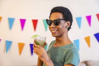 Portrait of a happy latin man with sunglasses drinking cocktail next to garlands decorating a house