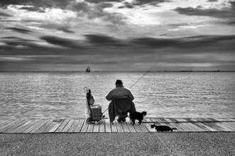 Fisherman, angler sitting on the promenade by the sea, cats, black and white, Thessaloniki,