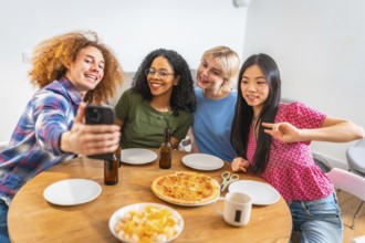 Four diverse friends are taking a selfie with a smartphone while enjoying lunch with pizza and beer