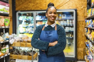 Smiling young african american saleswoman wearing an apron, standing confidently with arms crossed