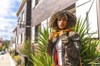 Latin woman in warm clothes standing outside a house in the street in a sunny day
