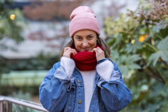 Young woman enjoying a winter day in the city, wearing a cozy pink beanie and a vibrant red scarf,