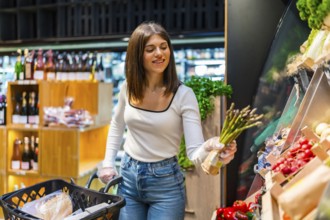 Young woman shopping for fresh asparagus in a supermarket, highlighting healthy eating habits and